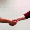 two person shaking hands near white painted wall